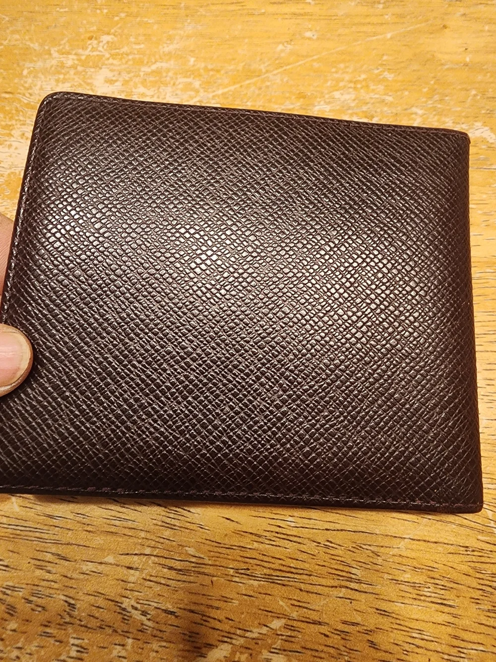 burgandy Louis Vuitton Taiga leather bifold wallet featuring a debossed LV